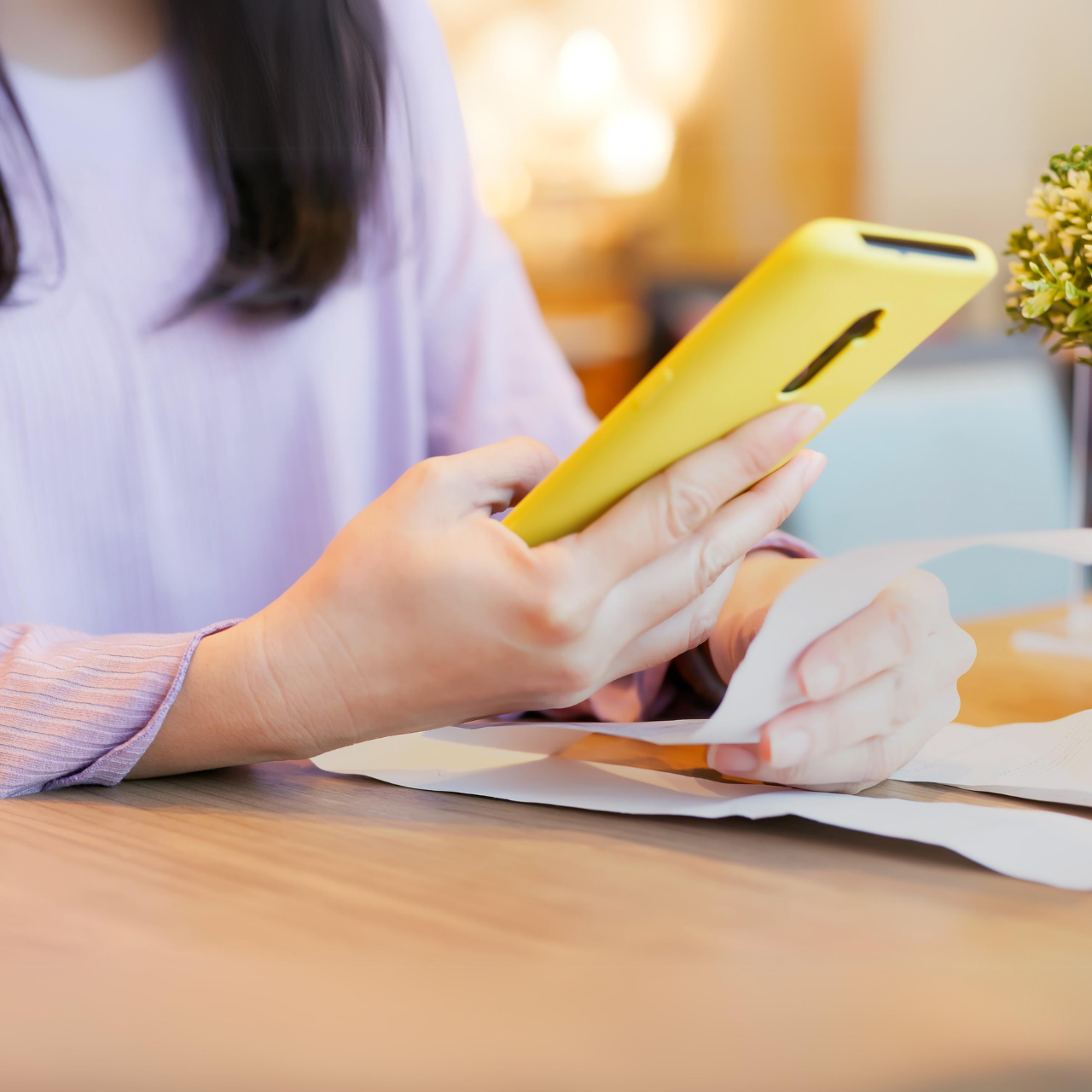A female customer is holding her phone to check an email receipt while also holding a paper receipt.