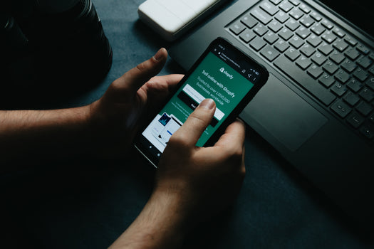Hands holding a smartphone displaying a Shopify page.