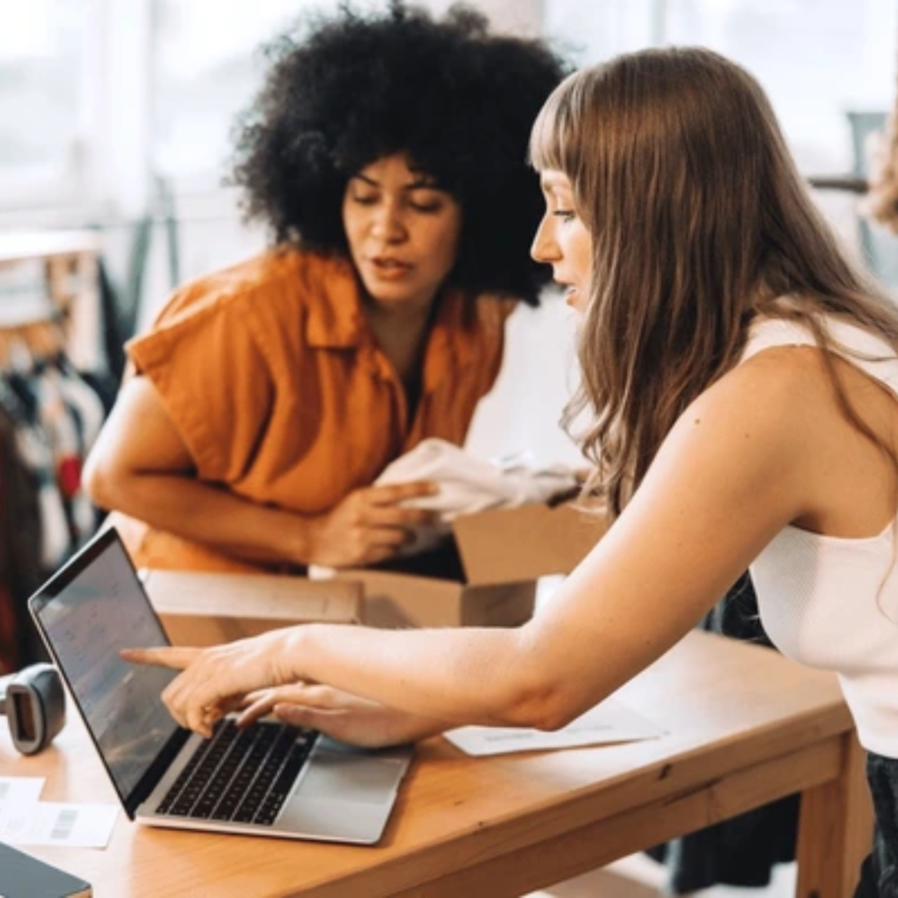 Two female clothing store owners are checking inventory on laptop.