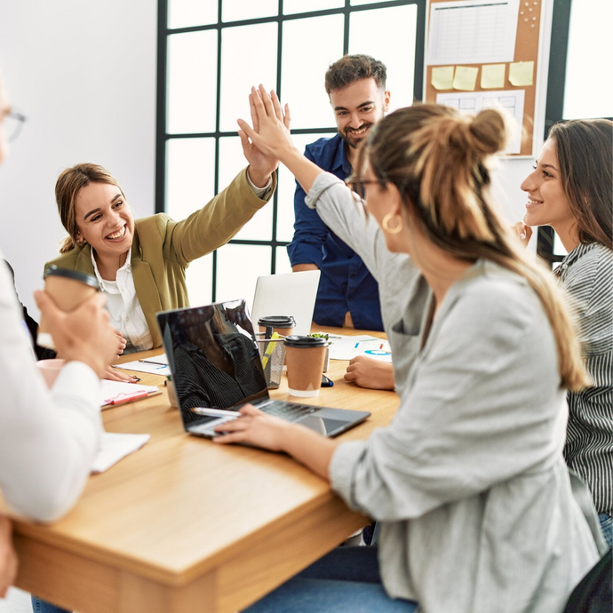 Members of two teams in a meeting room high-fiving each other.