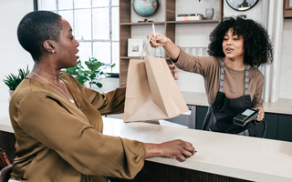 Retail staff packing a customer's purchase item into a shopping bag and handing them to the customer at the checkout counter.