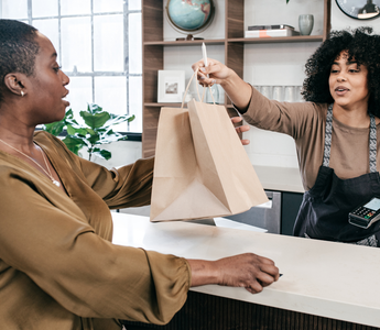 Retail staff packing a customer's purchase item into a shopping bag and handing them to the customer at the checkout counter.