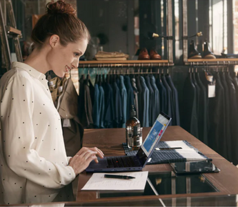 Clothing store owner reviewing online orders on a laptop at the checkout counter.
