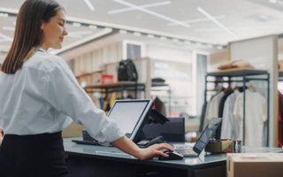 Female retail employee operating a POS system at a clothing store checkout counter.