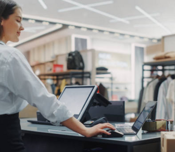 Female retail employee operating a POS system at a clothing store checkout counter.